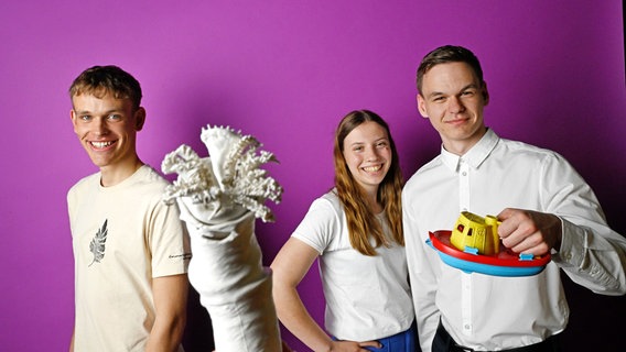 Drei junge Leute lächeln in die Kamera. Einer hält symbolisch ein Spielzeugboot in der Hand © Stiftung Jugend forscht e. V. 