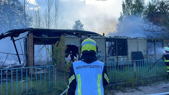 Ein Feuerwehrmann steht vor einer Lagerhalle in Güstrow, aus der Rauch wegen eines Brandes austritt. © Freiwillige Feuerwehr Güstrow Foto: Stephan Hagemann