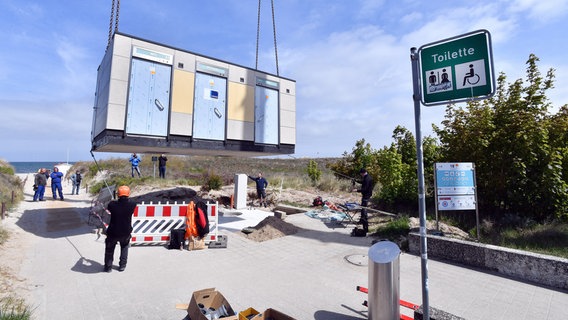 Ein Toilettenhäuschen wird an einem Kran an der Promenade in Warnemünde herunter gelassen. © Joachim Kloock Foto: Joachim Kloock