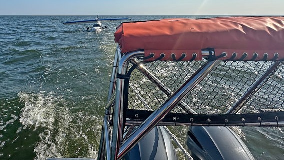 Blick über das Heck des Seenotrettungsboots "Eva Ahrens-Thies". Zwischen den zwei Außenbordmotoren verläuft eine Leine, an der ein Wasserflugzeug hängt. © Deutsche Gesellschaft zur Rettung Schiffbrüchiger Foto: Deutsche Gesellschaft zur Rettung Schiffbrüchiger