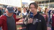 NDR Reporter Sven-Peter Martens steht mit einem Mikrofon neben einem älteren Mann. © NDR 