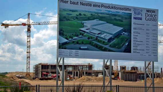 Das Baustellenschild mit einer Grafik des fertigen Nestlé-Werkes vor der Baustelle in Schwerin. © dpa-Bildfunk Foto: Jens Büttner