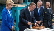 Wolgast: Bundesverteidigungsminister Boris Pistorius hält bei der Kiellegung der Fregatte F126 "Niedersachsen" auf der Peene-Werft einen Hammer in der Hand. Neben ihm stehen Manuela Schwesig (SPD, l), Ministerpräsidentin von Mecklenburg-Vorpommern, und Stephan Weil (SPD, 2.v.r), Ministerpräsident von Niedersachsen. © Stefan Sauer/dpa +++ dpa-Bildfunk +++ Foto: Stefan Sauer/dpa +++ dpa-Bildfunk +++