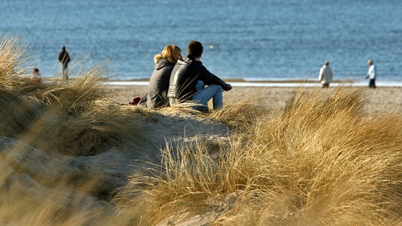 Zwei Menschen sitzen in der Sonne am Ostseestrand. © dpa Foto: Bernd Wüstneck