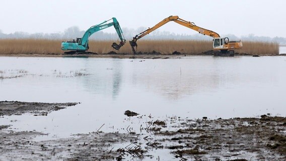 Zwei Bagger graben Erde am Rande einer Wasserfläche. © dpa-Bildfunk Foto: Bernd Wüstneck