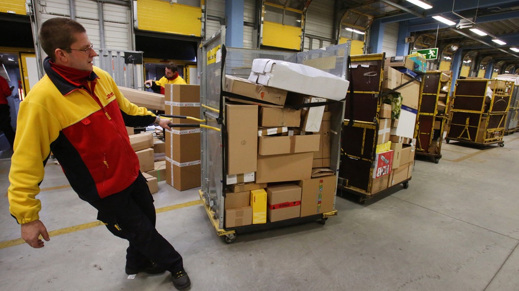 Ein DHL-Mitarbeiter zieht einen Container Pakete hinter sich her.