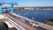Eine Luftaufnahme von der für Sanierungsarbeiten gesperrten Peenebrücke in Wolgast. Zu sehen sind eine Straßenfräse, die Material von der Brücke abträgt und dieses zeitgleich über ein Förderband in einen vorausfahrenden Lastwagen kippt. © NDR Foto: Thomas Eichler