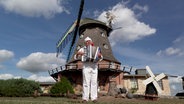 Ein Akkordeonspieler steht vor einer Windmühle. © NDR Foto: Screenshot