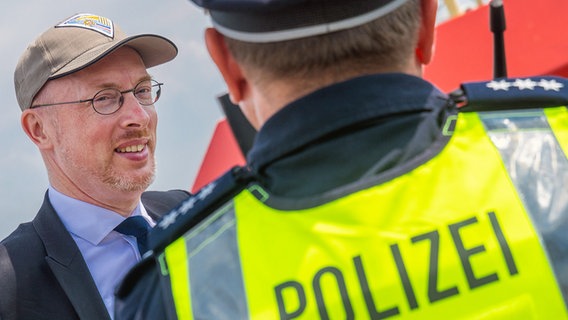 Mecklenburg-Vorpommerns Innenminister Christian Pegel (SPD, l) spricht mit einem Polizisten. © Jens Büttner/dpa Foto: Jens Büttner/dpa