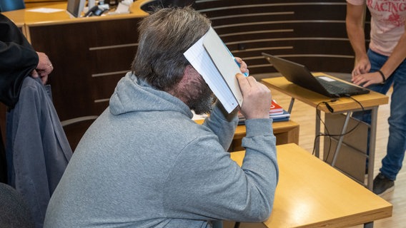 Stralsund: Der Angeklagte hält im Sitzungssaal im Landgericht einen Schreibblock vor sein Gesicht. © Stefan Sauer/dpa +++ dpa-Bildfunk +++ Foto: Stefan Sauer/dpa +++ dpa-Bildfunk +++