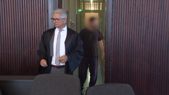 Ein Mann in schwarzer Robe und ein Angeklagter betreten den Gerichtssaal. (Archivbild Prozessauftrakt) © NDR Screenshot Foto: NDR Screenshot