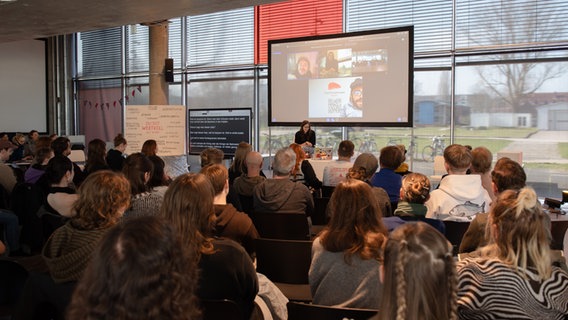 Zuschauer schauen auf eine Präsentation. Vor ihnen auf einer Leinwand ist Raúl Krauthausen zu sehen. © Hochschule Wismar Foto: Anna-Maria Siggelkow