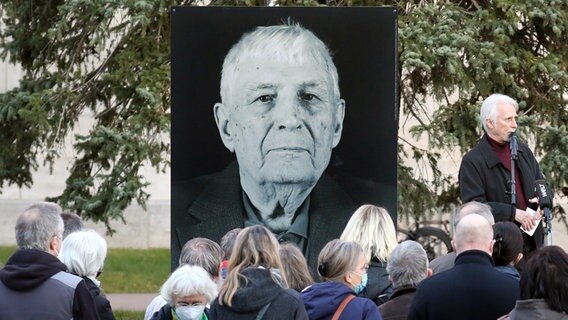 Weimar: Teilnehmer einer Gedenkstunde für den Buchenwald-Überlebenden Boris Romantschenko stehen vor dessen Foto. Der 96-jährige Boris Romantschenko wurde bei einem Bombenangriff in Charkiv getötet. ©  Bodo Schackow/dpa-Zentralbild/dpa Foto:  Bodo Schackow/dpa-Zentralbild/dpa
