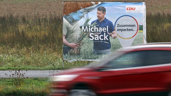 Ein vom Regen aufgeweichtes Wahlplakat für den Spitzenkandidat der CDU bei den Landtagswahlen in Mecklenburg-Vorpommern, Michael Sack, steht an einer Straße am Stadtrand Schwerins, im Vordergrund fährt ein rotes Auto vorbei. © dpa Foto: Jens Büttner