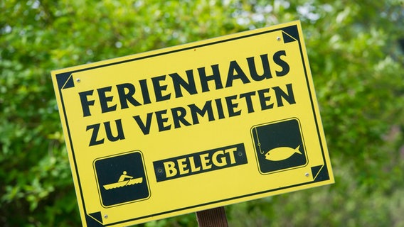 Vor einem Ferienhaus steht ein Hinweisschild mit dem Schriftzug "Ferienwohnung belegt". © dpa Foto: picture alliance / Stefan Sauer