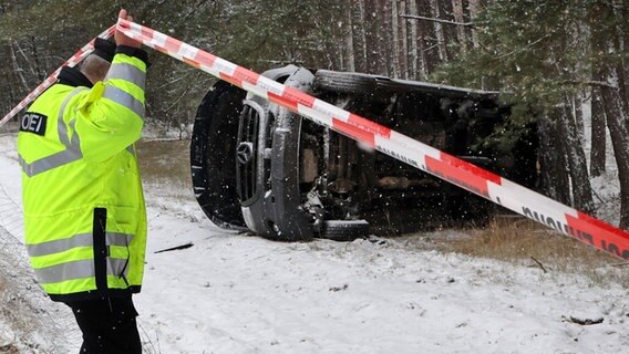 Polizist an einer Unfallstelle in Malchow - ein Transporter liegt nach einem Glätteunfall am Straßenrand © Bernd Wüstneck/dpa Foto: Bernd Wüstneck/dpa