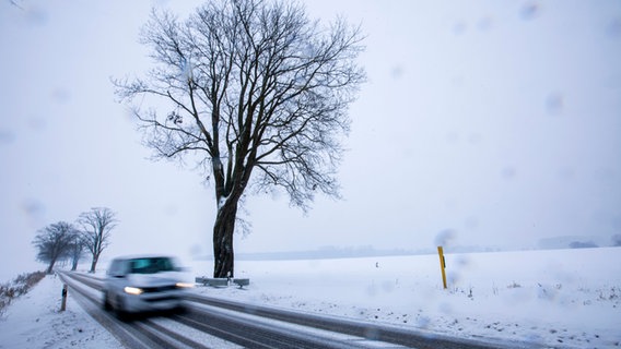 Ein Auto fährt auf einer verschneiten Straße in der Nähe von Groß Strömkendorf in Mecklenburg-Vorpommern.  © dpa Foto: Jens Büttner