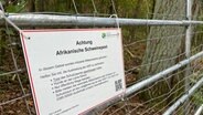 Afrikanisches-Schweinepest-Warnschild hängt an einem Zaun. © NDR Foto: Jürn-Jakob Gericke