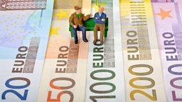 Zwei Rentner-Figuren sitzen auf einer Parkbank, die symbolisch auf Geldscheinen steht. © dpa-Zentralbild Foto: Eibner-Pressefoto