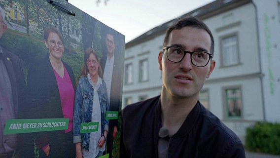 Grünen-Politiker Marcel Spittel neben einem Wahlplakat. © Screenshot 