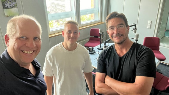 Fußballspieler Kai Pröger steht zwischen zwei Moderatoren in einem Radiostudio. Alle drei blicken lächelnd in die Kamera © NDR Foto: Tobias Blanck