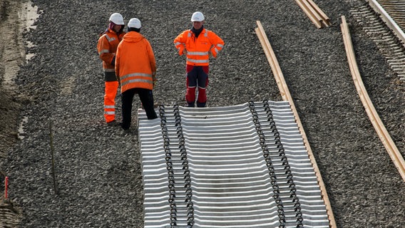 Drei Gleisarbeiter stehen auf der Baustelle einer Bahnstrecke © picture-alliance/dpa Foto: Bernd Wüstneck