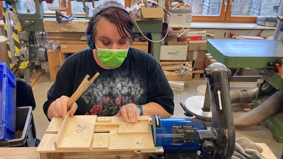 Frau mit Maske arbeitet an Werkbank.  