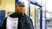 Verkäufer Torsten steht mit einem Exemplar der Straßenzeitung "Der Strohhalm" in Rostock vor einem Einkaufszentrum. © Frank Schlößer Foto: Frank Schlößer