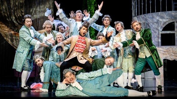 Zahlreiche Schauspieler posieren in historischer Garderobe auf der Bühne. Es ist die Besetzung von "La Cenerentola - Aschenputtel", einer Oper von Gioachino Rossini am Theater Vorpommern. © Peter van Heesen Foto: Peter van Heesen