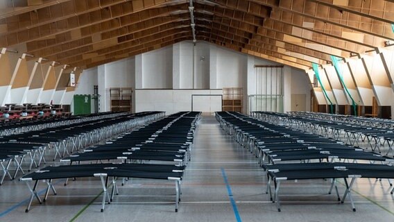 Sassnitz: In der Sporthalle Dwasieden stehen Feldbetten (fotografiert durch eine Glasscheibe).  Foto: Stefan Sauer/dpa