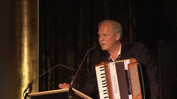 Der Schauspieler Ulrich Tukur spielt während der Preisverleihung des 30. Filmkunstfest Mecklenburg-Vorpommern im Schweriner Kino "Capitol" ein Lied auf seinem Akkordeon. © NDR Foto: Screenshot
