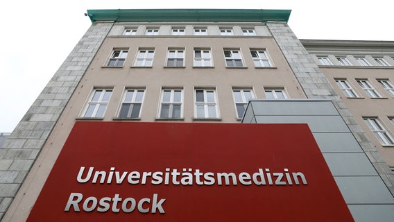 Ein Schild mit der Aufschrift "Universitätsmedizin Rostock" weist auf das entsprechende Gebäude im Hintergrund hin. © dpa-Bildfunk Foto: Bernd Wüstneck