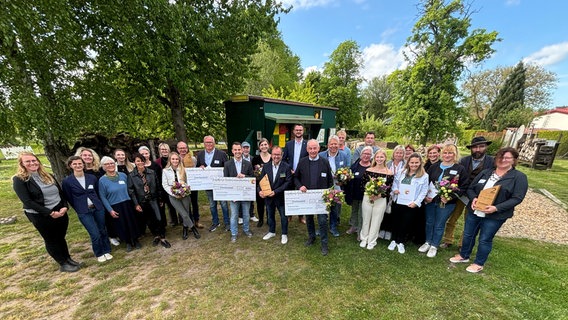 Etwa 30 Menschen stehen im Halbkreis und lächeln in die Kamera. Sie stehen auf einer grünen Wiese, vor einem Bienenwagen. Etwa 30 Menschen stehen im Halbkreis und lächeln in die Kamera. Sie stehen auf einer grünen Wiese, vor einem Bienenwagen. © Landkreis Nordwestmecklenburg Foto: Tore Degenkolbe