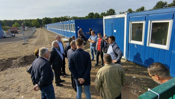 Vertreter des Kreistages von Nordwestmecklenburg stehen vor einem Container der Geflüchtetenunterkunft in Upahl. © NDR Foto: Christoph Woest