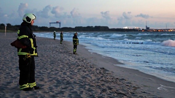 Rettungskräfte stehen in der Abenddämmerung am Strand und suchen die Ostsee nach einem Vermissten ab. © NDR Foto: Stefan Tretropp