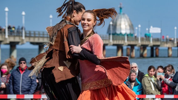 Die Schauspieler der Vorpommersche Landesbühne Anklam singen und tanzen am Strand auf der Insel Usedom. Im Hindergrund ist die Seebrücke zu sehen.  Foto: Stefan Sauer