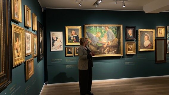 Henriette Maxin, Kunsthistorikerin und Kuratorin der Sonderausstellung "ErNEUt im Blick" steht vor mehreren Gemälden. © NDR Foto: Hannah Dautwiz