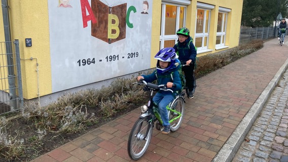 Zwei Kinder fahren mit dem Fahrrad an einer Schule vorbei. © NDR Foto: Susann Moll