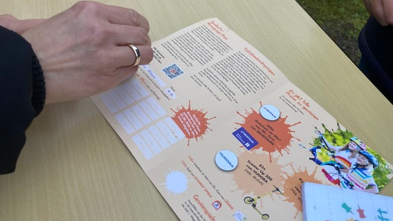 Ein Hand mit einem Stempel über einem Flyer. Ein Hand mit einem Stempel über einem Flyer. © NDR Foto: Susann Moll