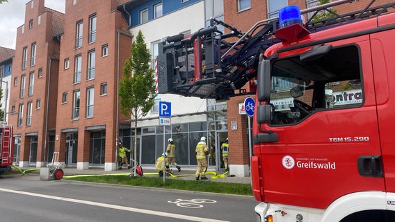 Blick vorbei an einem Feuerwerhrauto auf fünf Feuerwehrleute im Einsatz. © NDR Foto: Hannah Deutwiz