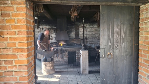 Ein Schmied steht in seiner Werkstatt und bearbeitet Metall. © NDR Foto: Pierre Sens