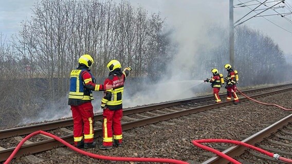 Vier Feuerwehrleute löschen einen Brand an den Gleisen. © Freiwillige Feuerwehr Gemeinde Neuenkirchen 
