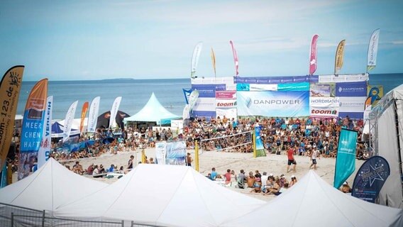 Menschen sitzen am Strand an einem Beachvolleyballfeld. Im Hintergrund ist die Ostsee zu sehen. © NDR Foto: Johannes Kasch