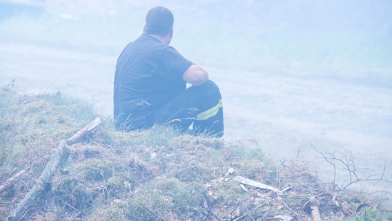 Ein erschöpfter Feuerwehrmann sitzt in einer Rauchwolke im brennenden Wald in der Nähe der kleinen Ortschaft Alt Jabel. © dpa-Bildfunk Foto: Jens Büttner