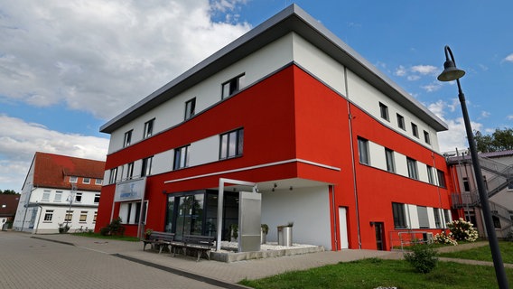 Blick bei blauem Himmel auf die Warnow-Klinik von außen. Ein quadratischer, modern wirkender Bau in rot und weiß mit einer kleinen Rasenfläche. © dpa Bildfunk Foto: Bernd Wüstneck