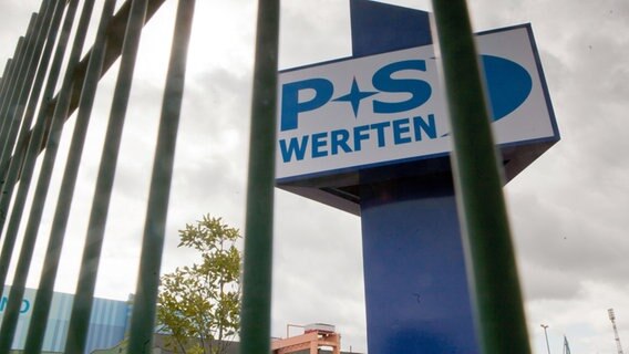 Das Firmenschild der P+S-Werften ist am Eingang zur Volkswerft in Stralsund hinter einem Zaun zu sehen. © dpa-Bildfunk Foto: Jens Büttner