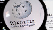 Unter einer Lupe ist der Schriftzug und das Logo des Online-Lexikons Wikipedia auf einem Computerbildschirm zu sehen. © dpa-Bildfunk Foto: Jens Büttner