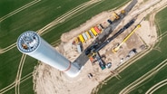 Der erste Teil einer insgesamt 238 Meter hohen Windkraftanlage steht in Questin. Drohnenaufnahme vom Aufbau. © Jens Büttner/dpa Foto: Jens Büttner/dpa