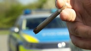 Ein Joint qualmt vor einem Polizeiauto. © NDR 