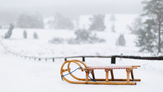 Ein Holzschlitten vor einer verschneiten Winterlandschaft im Büsenbachtal nahe Buchholz in der Nordheide. © Alexander Cornelius Mühlhausen 